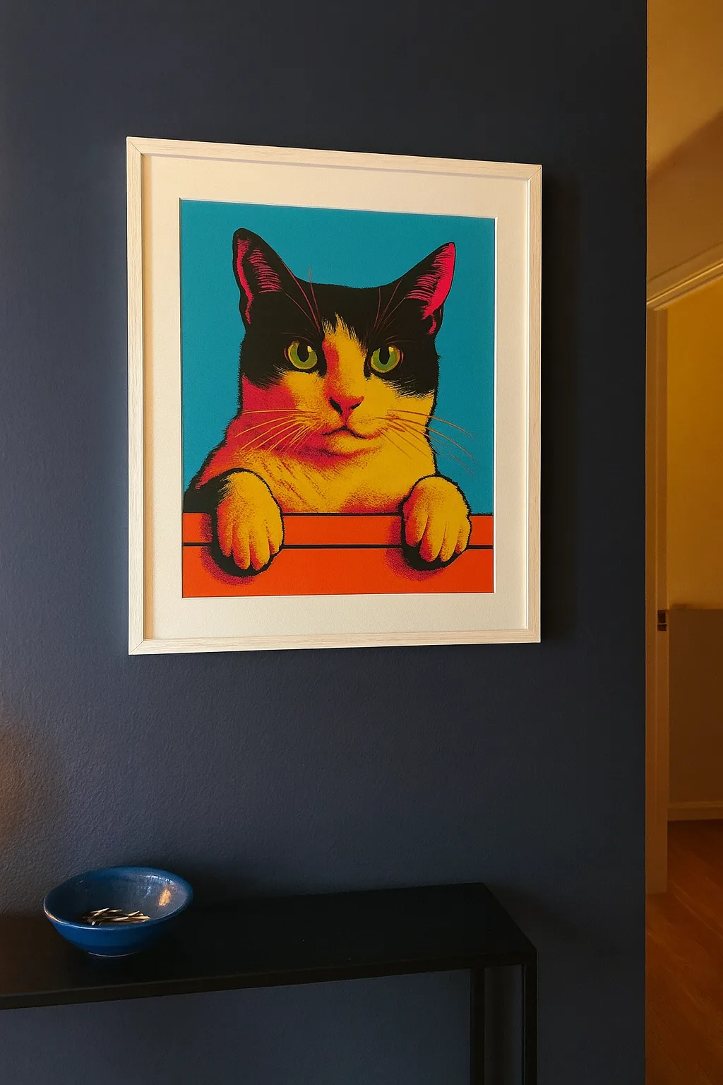 A white-framed pop-art cat portrait hanging on a dark navy hallway wall